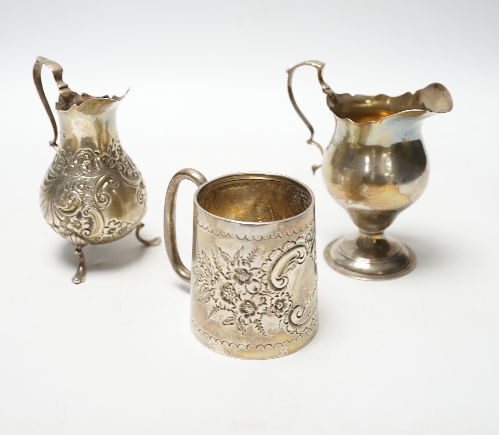 A Victorian silver inverted pyriform cream jug, London, 1886, 10.4cm, another, embossed, Chester, 1896 and an Edwardian silver embossed christening mug, Chester, 1902, 8.1oz.